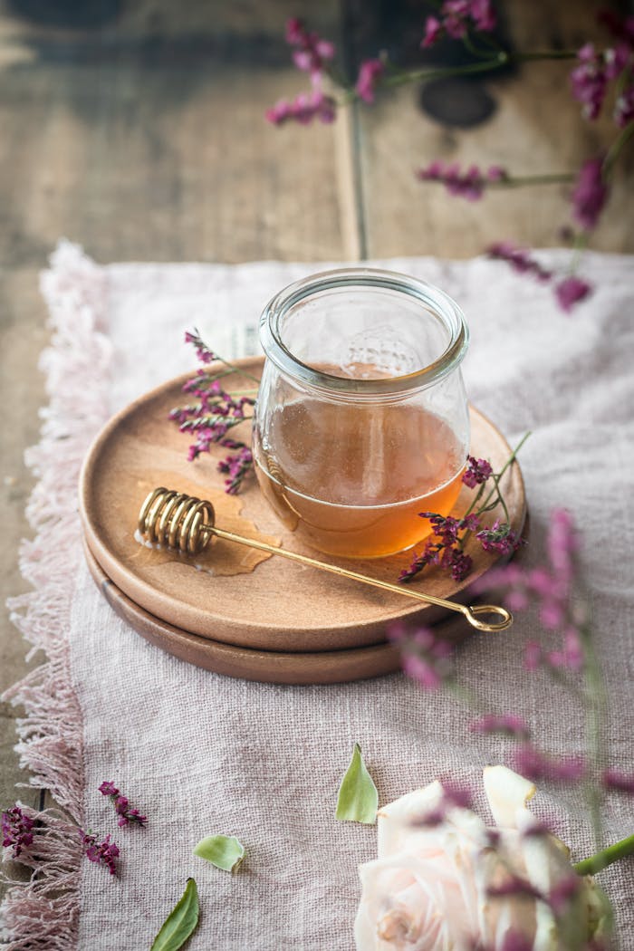 A rustic still life of a honey jar, gold dipper, and flowers on a wooden table.